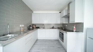 Eine moderne Küche mit weißen Schränken, einer grauen gefliesten Spritzschutzwand, Edelstahlgeräten und einer grauen Holz Arbeitsplatte.