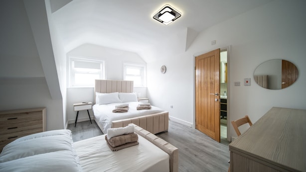 Ein Schlafzimmer mit einem großen Bett, einem Nachttisch, einem Sessel und einer Holztür.