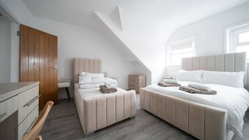 Une chambre moderne avec un plafond en pente, deux lits avec des têtes de lit assorties, une porte en bois et une petite table de chevet.