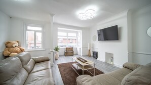 Ein modernes Wohnzimmer mit einer Couch, einem großen Teddybären, einem Kamin und einem an der Wand befestigten Fernseher.