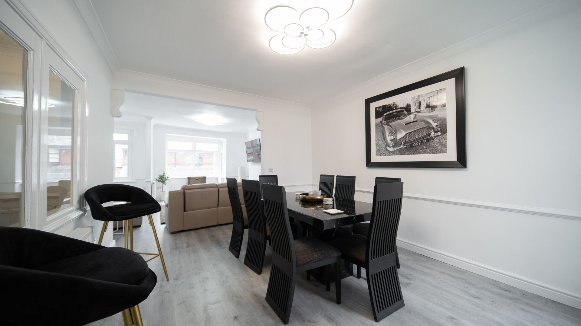 Un coin repas avec une table noire, six chaises et une photographie en noir et blanc encadrée représentant une voiture, accroch ée au mur.