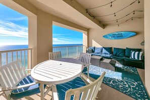 A balcony with a round table and chairs, a sofa with blue cushions, and a sign reading "TAYLOR'S EST. 1999". - Grand Panama 1-1807 (Panama City Beach)