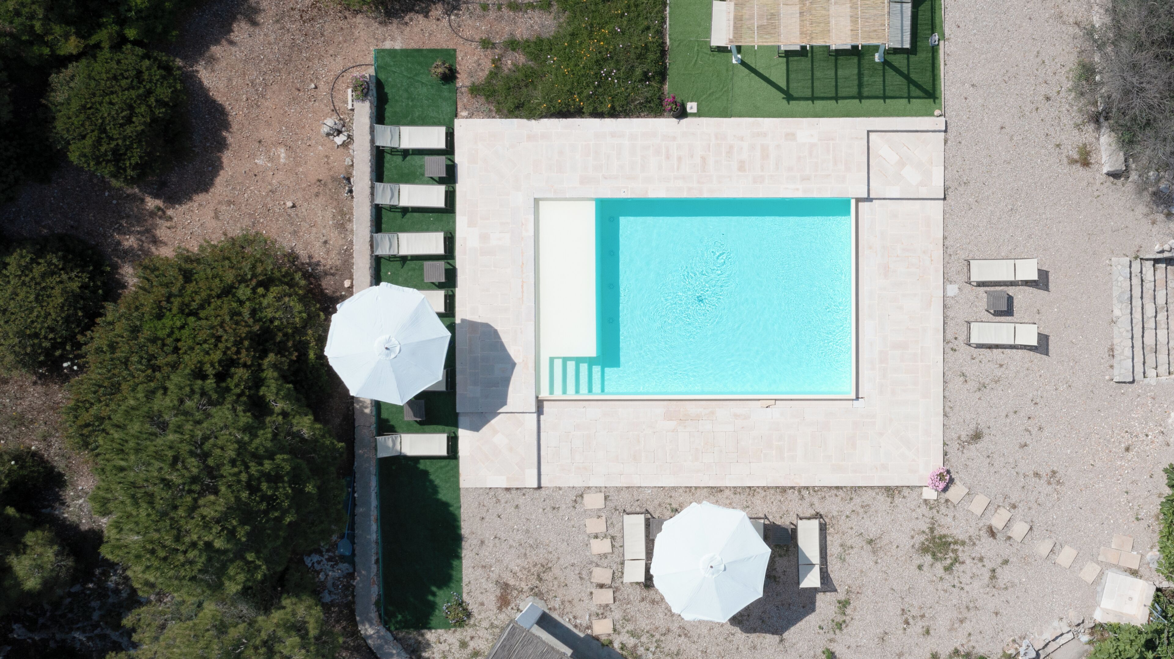 An aerial view of a pool area with a rectangular pool, surrounding lounge chairs, and umbrellas.