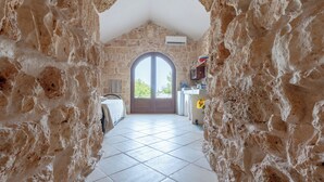 A stone-walled corridor leading to a room with a tiled floor and a large arched doorway.