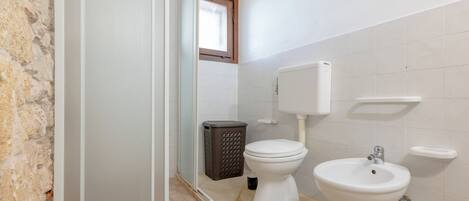 Een badkamer met toilet, bidet, wastafel, afvalbak en een douchehoek.
