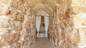 A stone corridor with a bed at the end, featuring a canopy.
