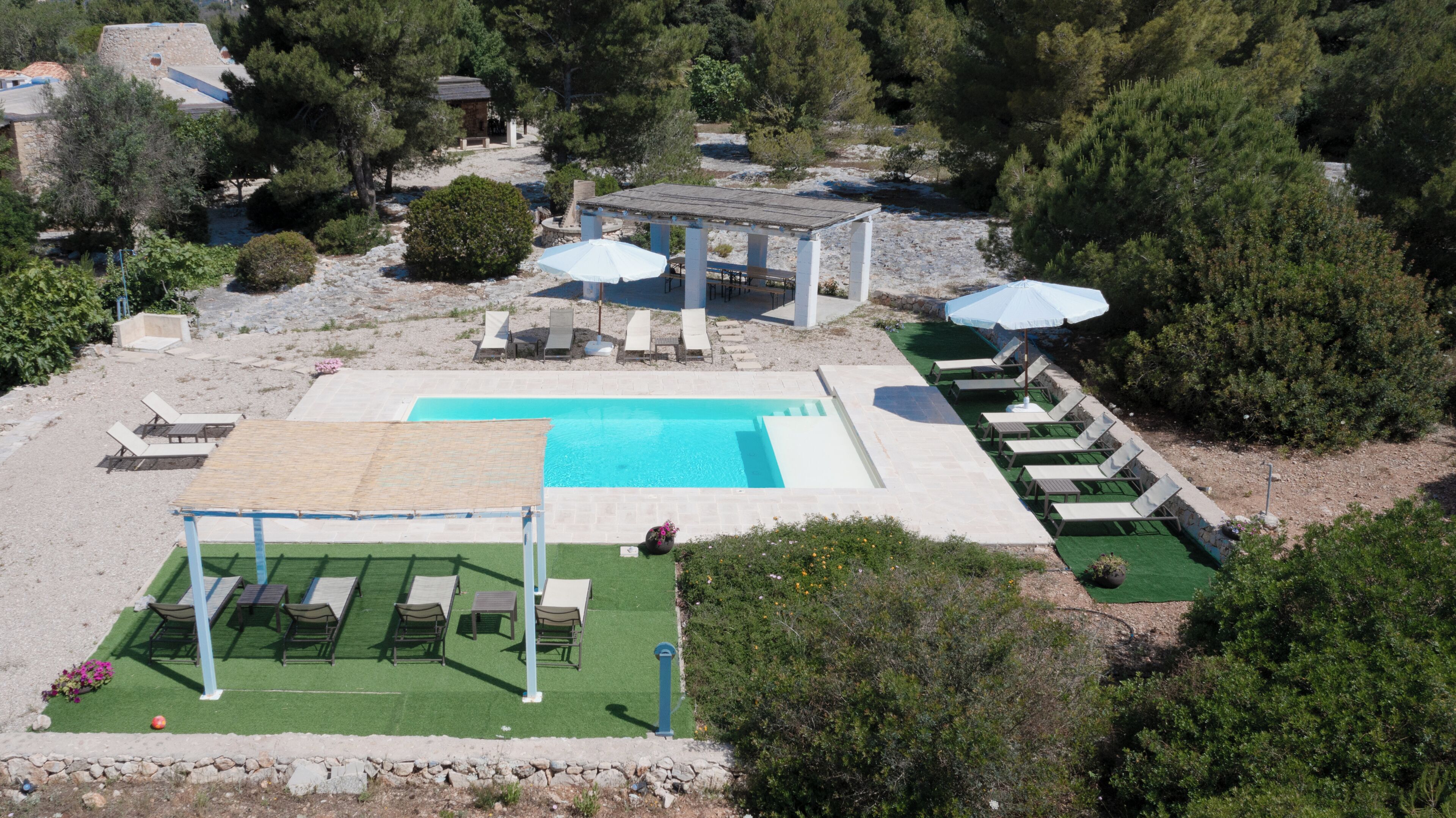 A pool area with lounge chairs, a pergola, and a small garden.