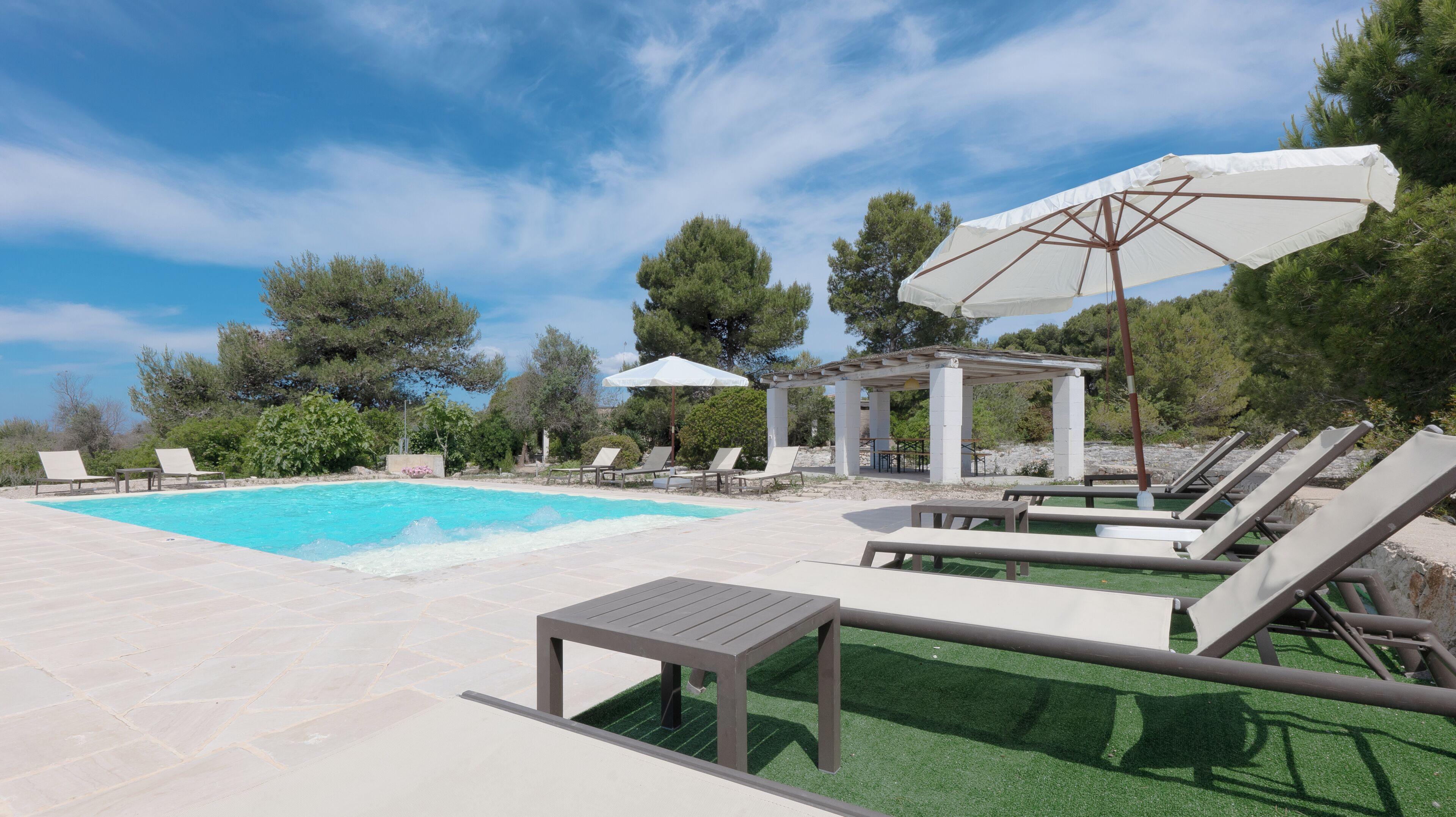 Una piscina con sillas de descanso y una pérgola.