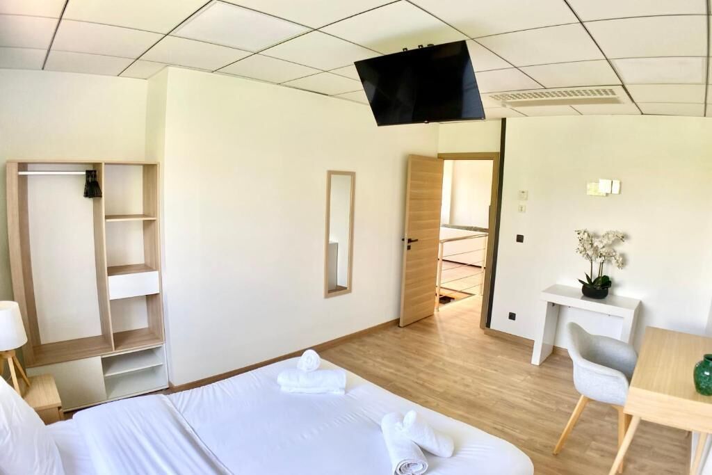 Ett hotellrum med en säng, ett skrivbord, en stol, en TV, en garderob och en spegel.