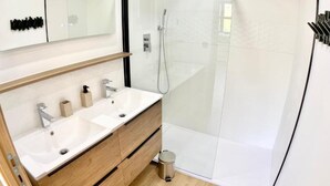 A modern bathroom with a double sink vanity, a glass shower enclosure, and a small trash bin. - New house Ovalie Montpellier near Stade de Rugby (Montpellier)