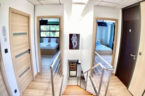 Un couloir d’hôtel moderne, avec un plancher en bois, un escalier central et des portes donnant accès aux chambres.