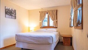 Un dormitorio con cama, mesita de noche, lámpara, ventana con cortinas e imagen en la pared.