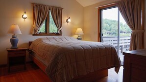 A bedroom with a large bed, two bedside lamps, a window with curtains, and a view of a balcony. - Come stay at our four season resort! (Weare)
