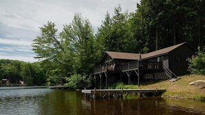 A cabin with a dock extending into a lake, surrounded by dense forest. - Come stay at our four season resort! (Weare)