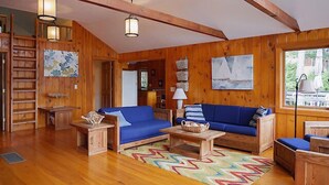 A wooden cabin interior with a blue sofa, wooden tables, and a colorful rug. - Come stay at our four season resort! (Weare)