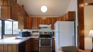 A compact kitchen with wooden cabinets, a stove, a refrigerator, and a window providing natural light. - Come stay at our four season resort! (Weare)