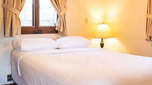 A bed with white bedding, a bedside lamp, and a window with curtains. - Come stay at our four season resort! (Weare)