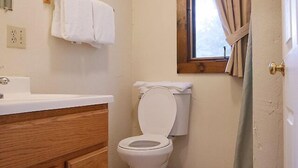 A bathroom with a white toilet, a wooden vanity, a white sink, and a window with curtains. - Come stay at our four season resort! (Weare)