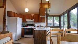 A compact kitchen with wooden cabinets, a refrigerator, stove, and a dining area with wooden chairs. - Come stay at our four season resort! (Weare)