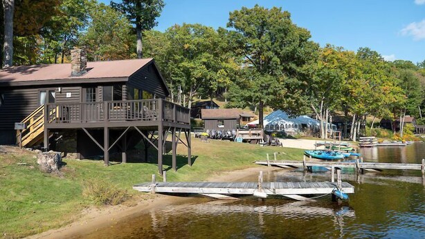 A lakeside cabin with a deck, dock, and boats. - Come stay at our four season resort! (Weare)