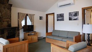 A cozy living room with a stone fireplace, a television, a sofa, and a lamp. - Come stay at our four season resort! (Weare)
