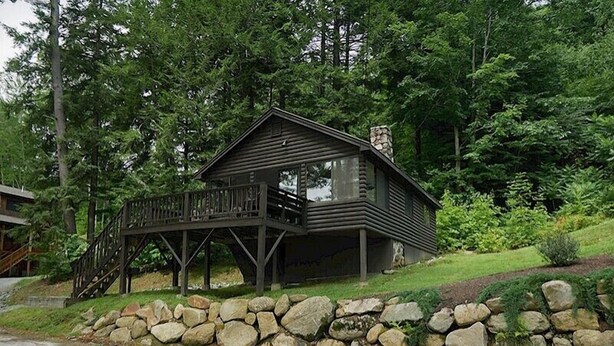 A cabin with a wooden deck and stone foundation, surrounded by lush greenery. - Come stay at our four season resort! (Weare)