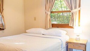 A neatly made bed with white linens, a wooden nightstand with a lamp, and a window with curtains. - Come stay at our four season resort! (Weare)