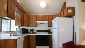 A compact kitchen with wooden cabinets, a white stove, a microwave, and a refrigerator. - Come stay at our four season resort! (Weare)