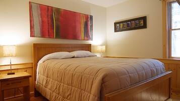 A bedroom with a wooden bed, two bedside tables, a large abstract painting, and a framed photo collection on the wall.