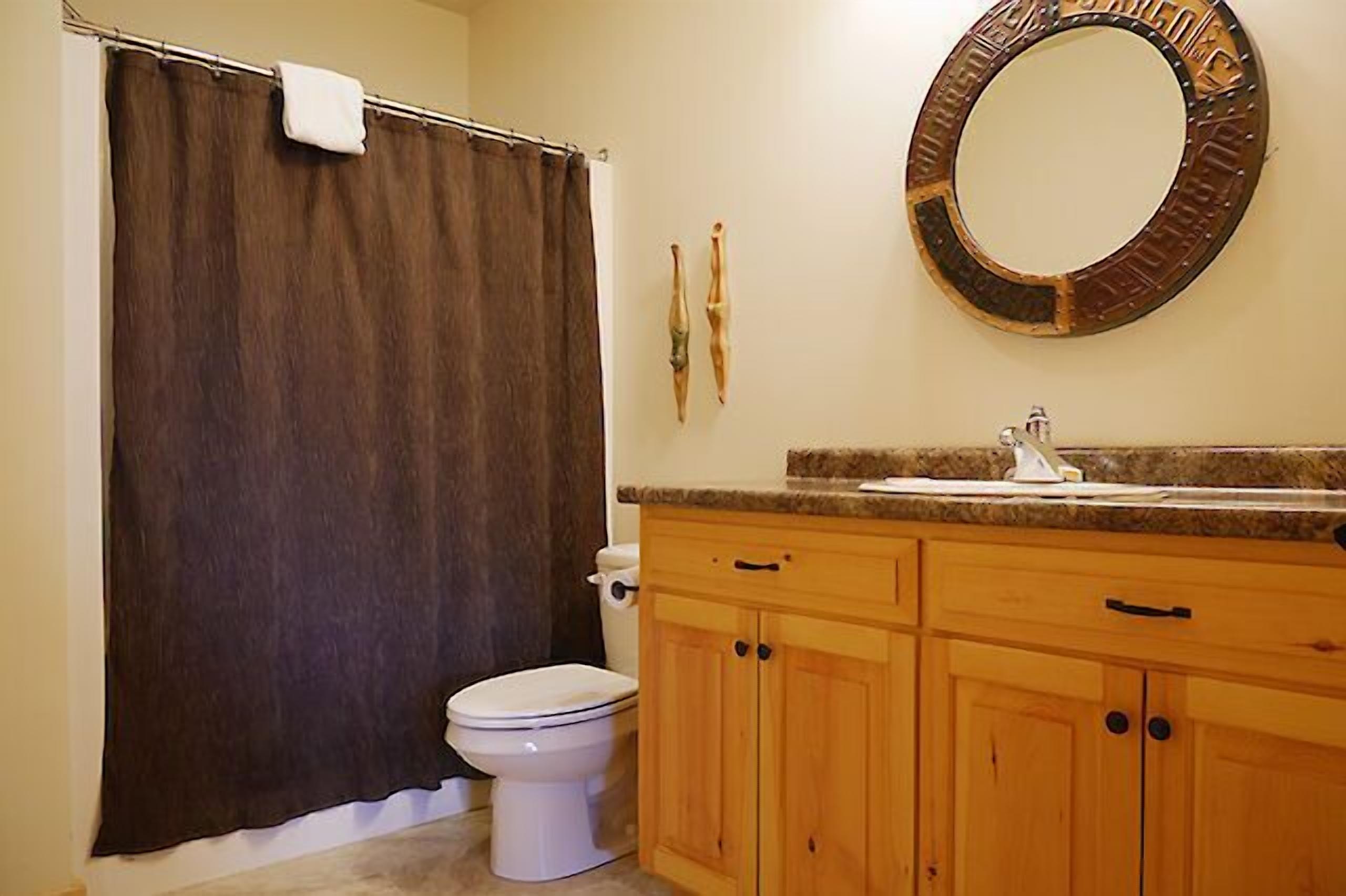 Een badkamer met douchegordijn, toilet, houten kastjes en een wastafel met spiegel erboven.