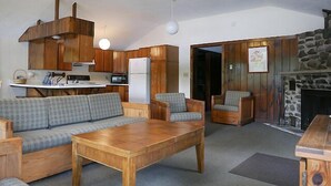 Uma sala de estar acolhedora com sofá, cadeiras, mesa de centro de madeira, lareira e área de cozinha com armários e eletrodomésticos de madeira.
