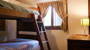 Quarto com beliche, escada, janela com cortinas e escrivaninha com luminária.