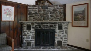 Uma lareira de pedra com porta de vidro preto, emoldurada por painéis de madeira e uma parede de pedra.