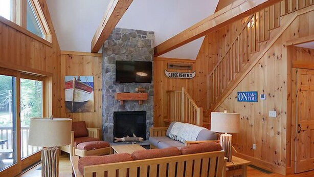 L’intérieur chaleureux d’un chalet avec une cheminée en pierre, des meubles en bois et un panneau indiquant « Location de canoës ».