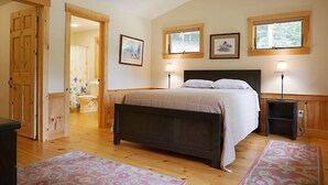 A bedroom with a bed, two bedside lamps, a wooden headboard, and a window with a view of trees. - Come stay at our four season resort! (Weare)