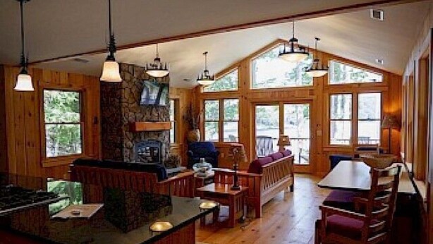 A cozy cabin interior with a kitchen area, wooden dining table, and large windows offering views of the outdoors. - Come stay at our four season resort! (Weare)