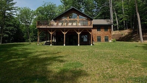 A two-story wooden cabin with a balcony, surrounded by a grassy area and trees. - Come stay at our four season resort! (Weare)