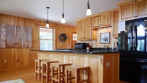 A kitchen with wooden cabinets, a black refrigerator, a microwave, and a bar area with stools. - Come stay at our four season resort! (Weare)
