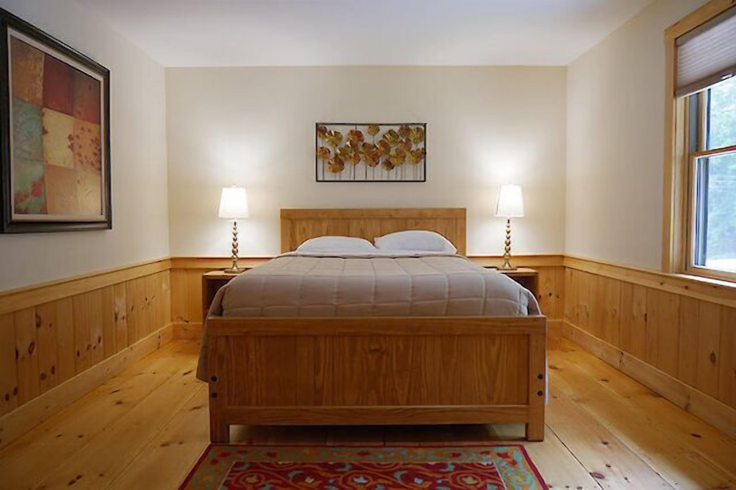 A wooden bed in a room with a window and two wall-mounted lamps.