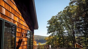 A wooden cabin with a deck, large windows, and a view of a lake surrounded by trees. - Come stay at our four season resort! (Weare)