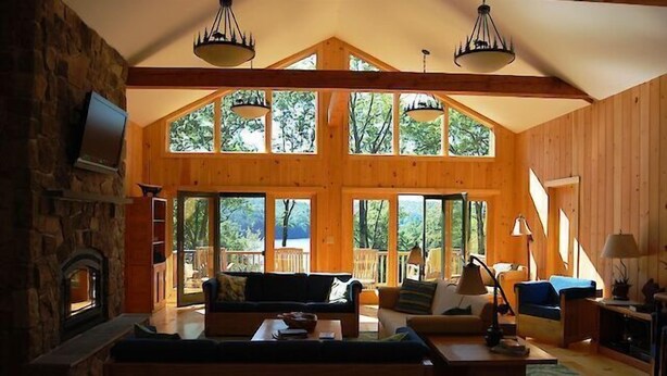 A spacious living room with a stone fireplace, wooden beams, large windows, and a cozy seating area. - Come stay at our four season resort! (Weare)