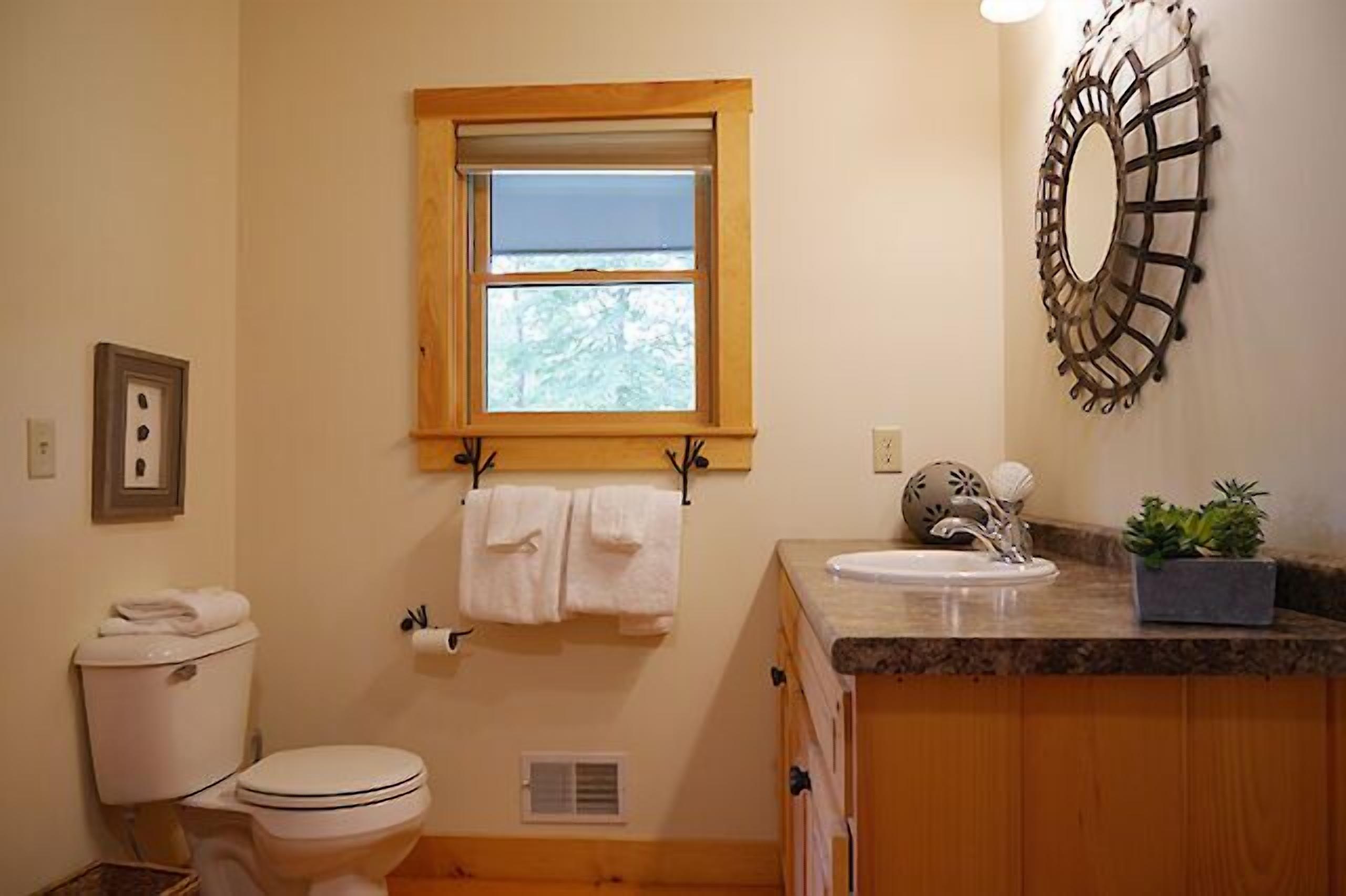 A bathroom with a toilet, sink, window, towel rack, and decorative wall piece.