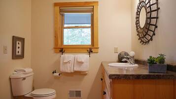 A bathroom with a toilet, sink, window, towel rack, and decorative wall piece.
