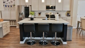 A modern kitchen with a central island, bar stools, stainless steel appliances, and pendant lighting.