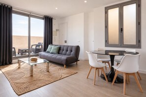 A modern living room with a sofa, a glass coffee table, and a dining area with a table and chairs. - Sweett | Symphonic Central Atico 2 (Barcelona)