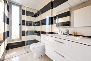 A modern bathroom with a glass-enclosed shower, a white toilet, and a vanity with a mirror. - Sweett | Symphonic Central Atico 2 (Barcelona)