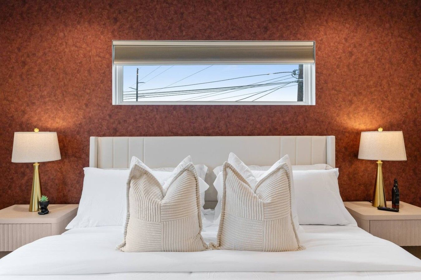 Une chambre d’hôtel avec un grand lit, deux tables de chevet et une fenêtre donnant sur des lignes électriques.