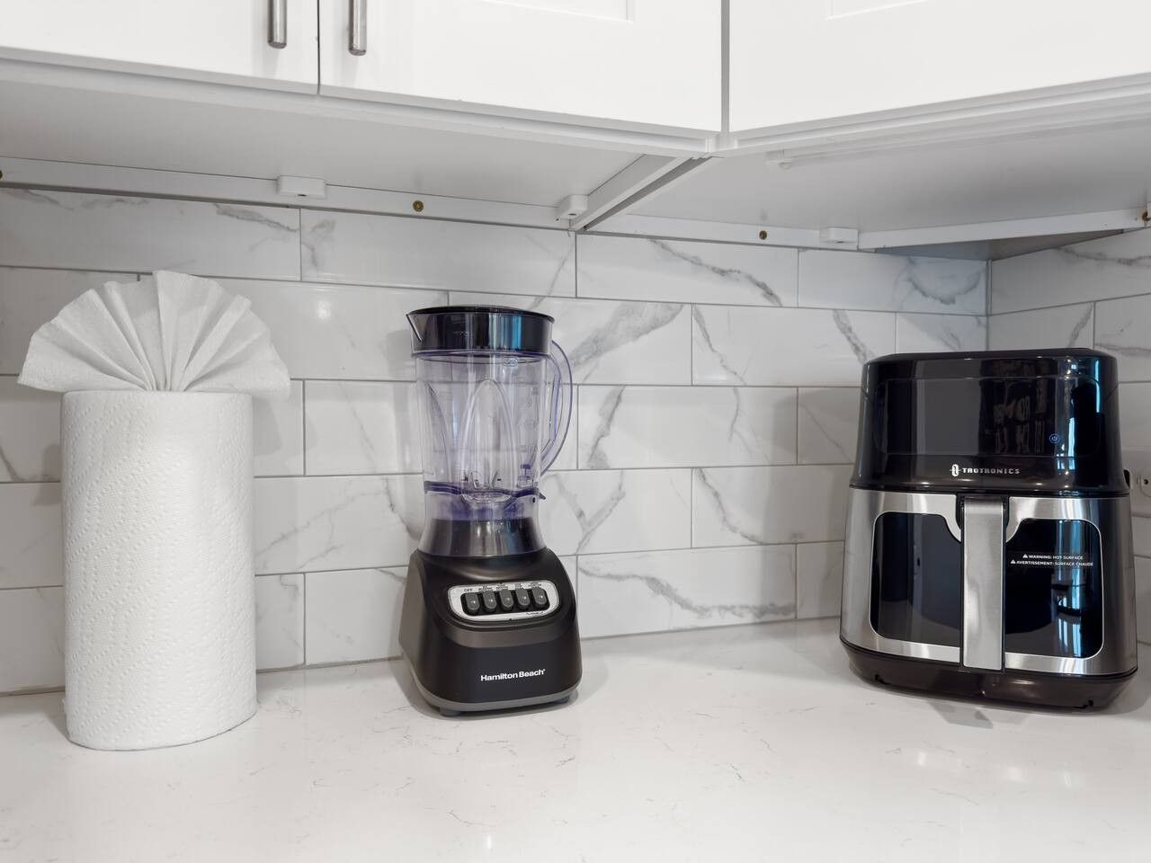 Eine Küche mit einem Mixer, einer Kaffeemaschine und einem Papiertuchhalter auf einer weißen Arbeitsplatte.