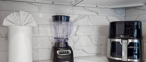 A kitchen with a blender, a coffee maker, and a paper towel holder on a white countertop.