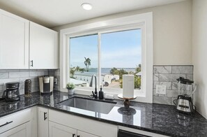 A kitchen with a large window, a sink, and a countertop with a coffee maker and a blender. - Entire 6BR Beach Duplex | Walk to Beach | Sleeps 12 (Bradenton Beach)